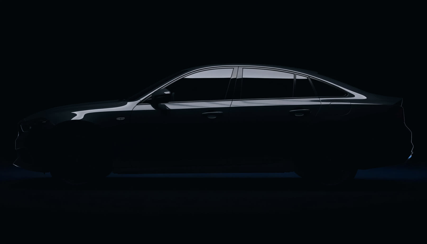 A dark sedan in a studio with a single light raking along its flank, revealing an unbroken reflection in the paint