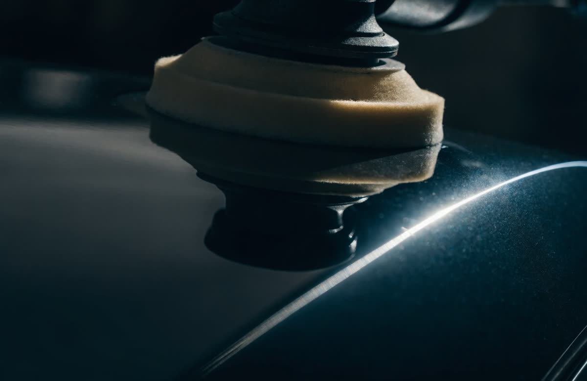 A dual-action polisher spreading polish across a deep black car panel, leaving a mirror finish