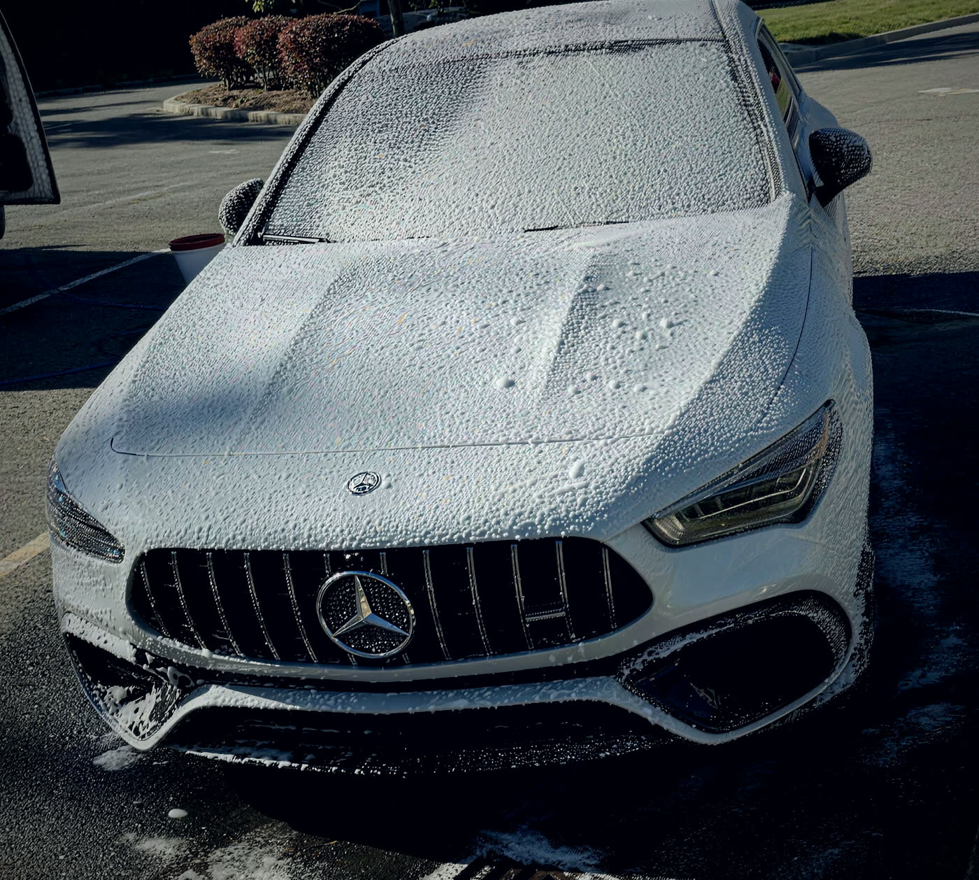 Mercedes-AMG GT four-door coupe covered in thick foam-cannon pre-wash on a parking lot