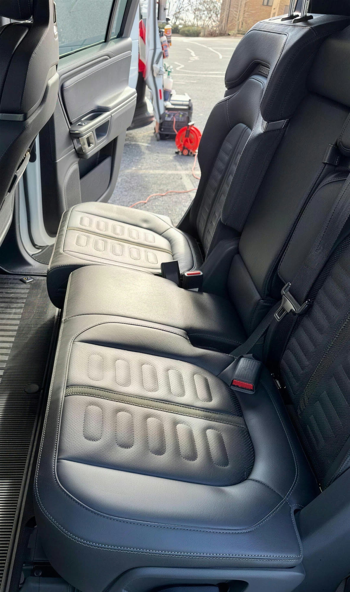 Second-row black leather seats of a large SUV cleaned during a mobile detail, with detailing equipment and a generator on the pavement outside
